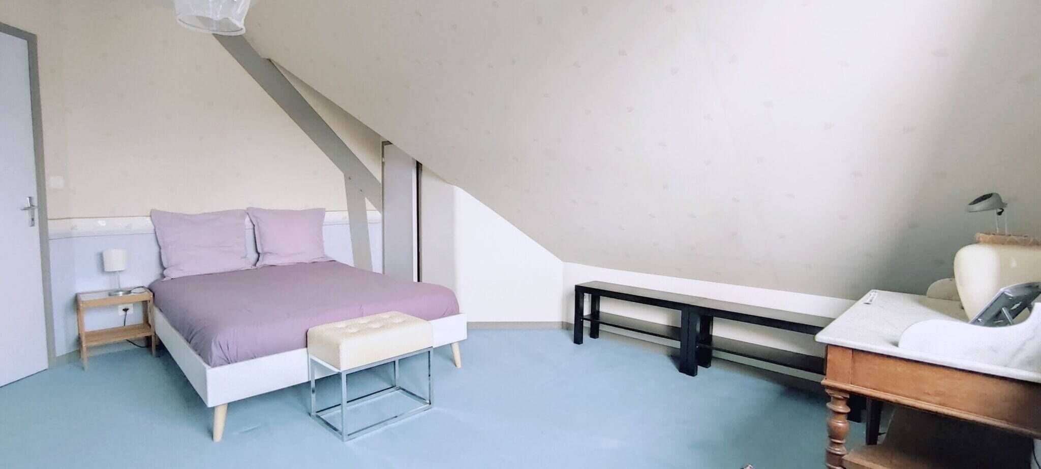 A bedroom with a bed, bedside table, lamp, bench, and a desk with a chair.