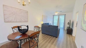 A living room with a sofa, a dining table with chairs, and a chandelier. - Cozy 2BR condo at River Oaks (Myrtle Beach)