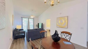 A living room with a sofa, a dining table with chairs, a chandelier, and a TV. - Cozy 2BR condo at River Oaks (Myrtle Beach)