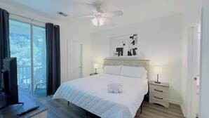 A hotel room with a large bed, a ceiling fan, a TV, and a balcony with curtains. - Cozy 2BR condo at River Oaks (Myrtle Beach)