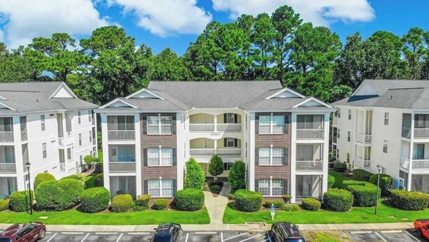 A multi-story residential building with balconies, a central courtyard, and a parking lot. - Cozy 2BR condo at River Oaks (Myrtle Beach)