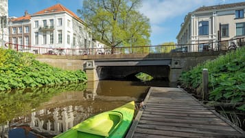 A canal with a green boat docked on a wooden pier, a bridge, and buildings with balconies.