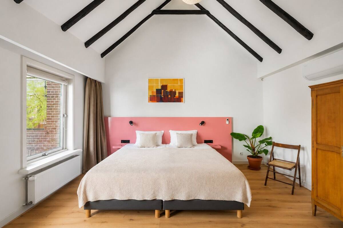 Un dormitorio con cama, ventana, planta en maceta, una silla y un armario de madera.