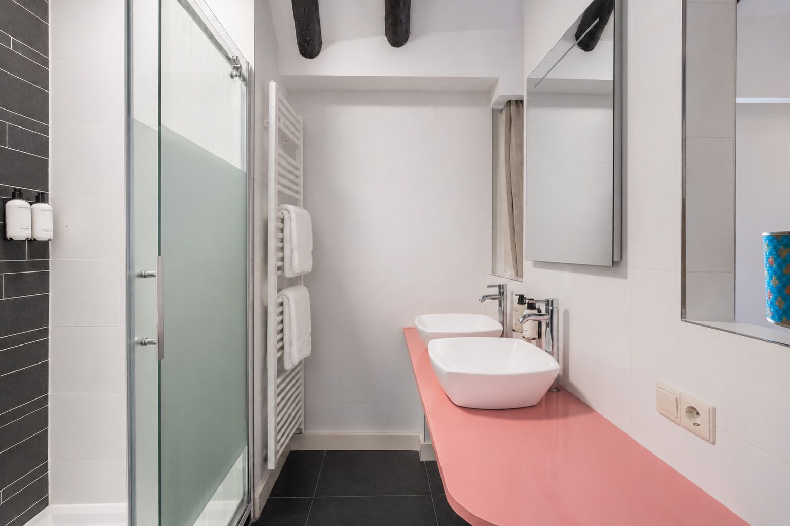 A modern bathroom with two sinks, a glass shower enclosure, and a pink countertop.