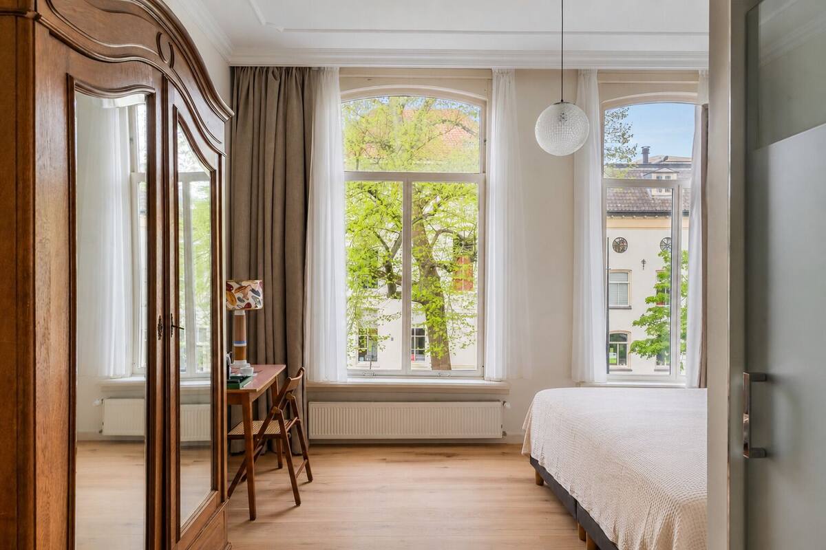Un dormitorio con un ventanal grande, una cama, un escritorio con silla y un armario.