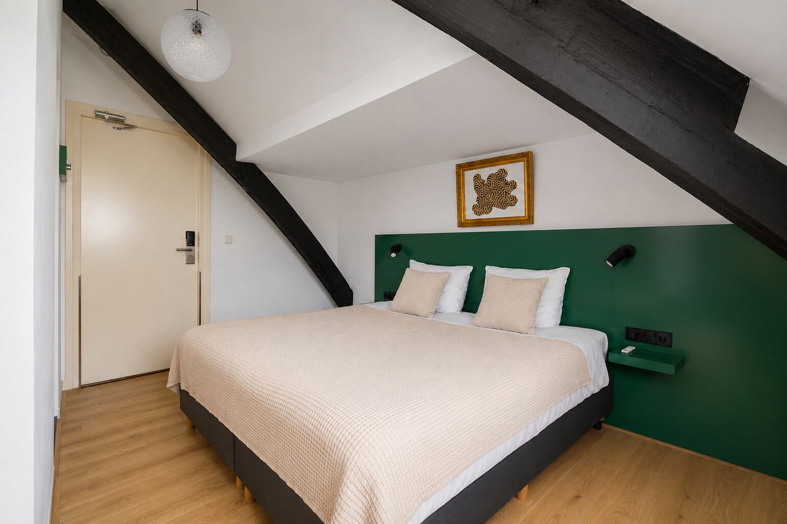 Un dormitorio con techo inclinado, cama con cabecera verde, una puerta y un aplique de pared.