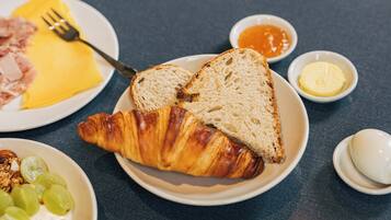 Une table dressée pour le petit-déjeuner avec des croissants, des toasts, du jambon et des fruits sur des assiettes.