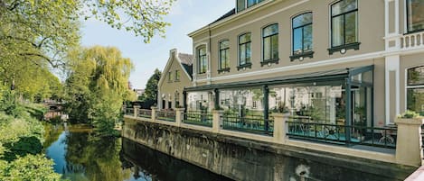 Un edificio a orillas de un canal con un añadido de cristal, un puente y un reflejo en el agua.