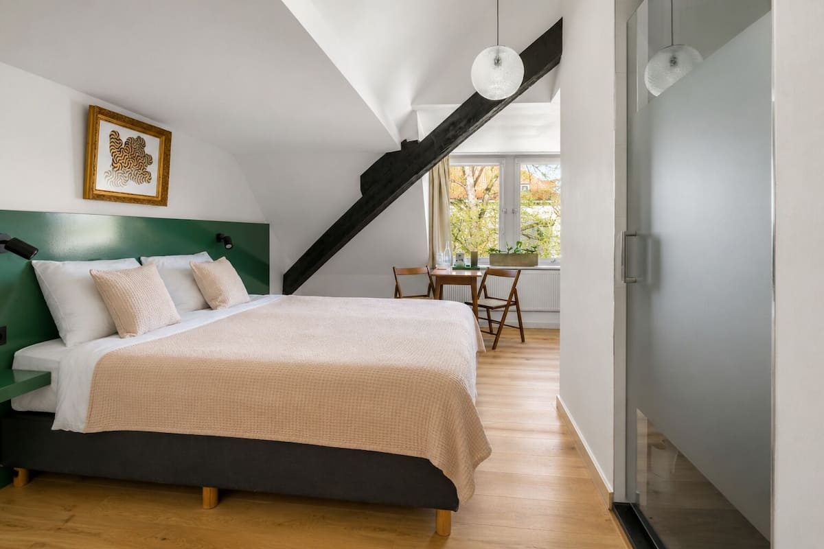 Un dormitorio con cama, escritorio y ventana con vistas a árboles.