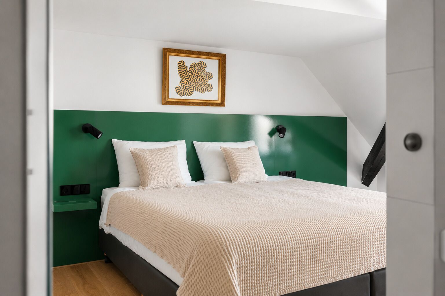 A bedroom with a bed, two bedside tables, a green accent wall, and a framed artwork above the bed.