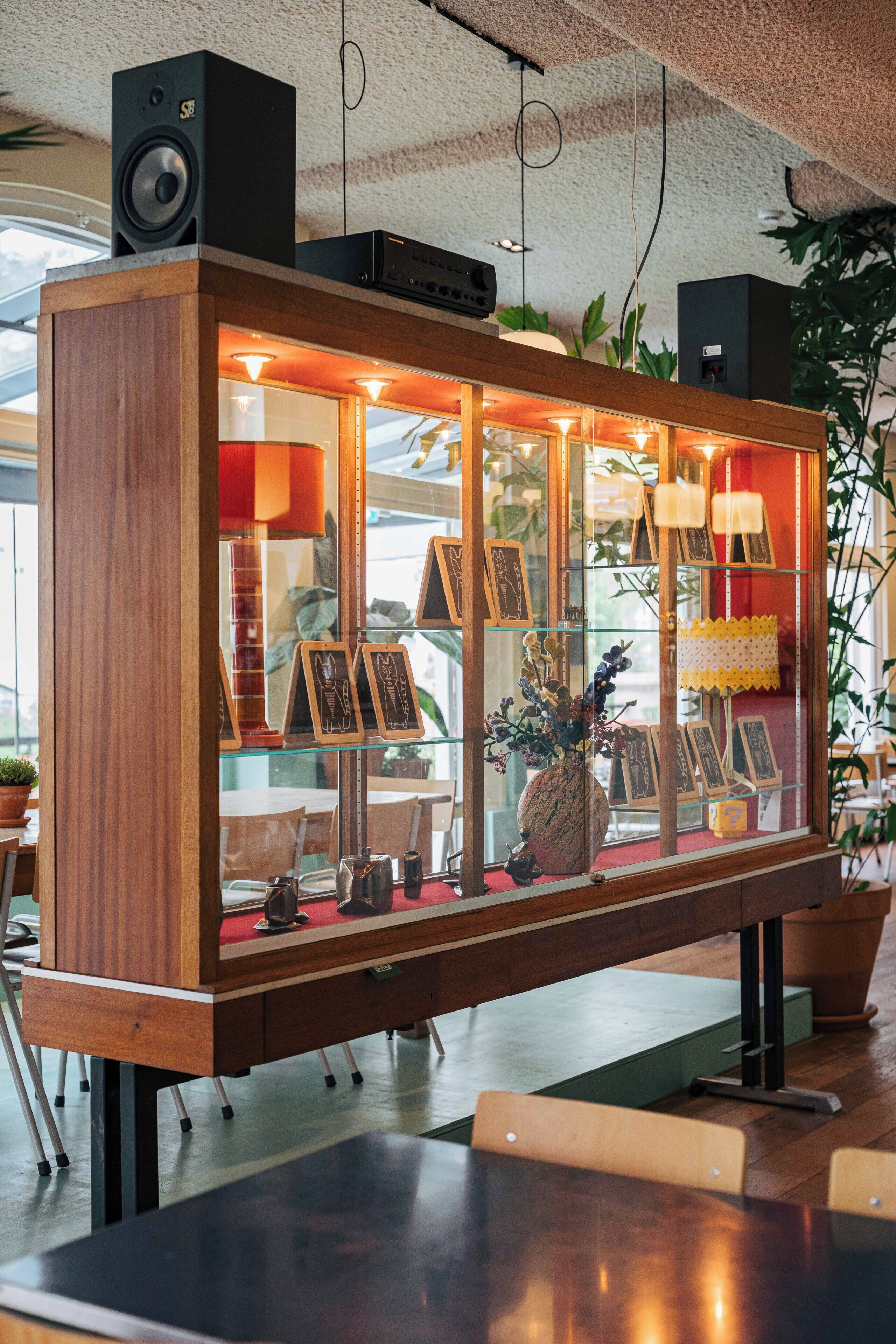Un mueble de madera con puertas de cristal, que contiene cuadros enmarcados y objetos decorativos.