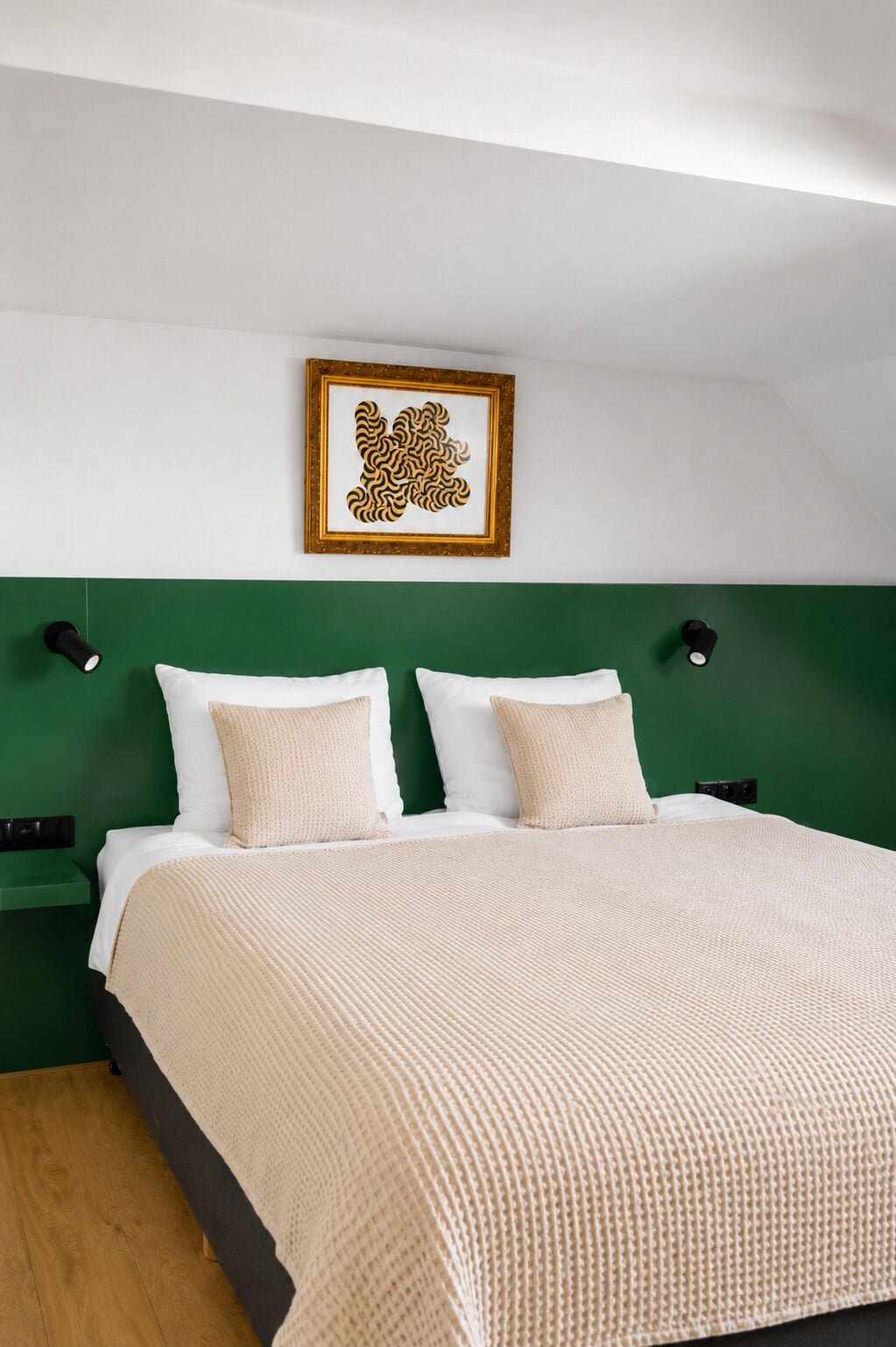Un lit avec une tête de lit verte, deux tables de chevet, une œuvre d’art encadrée au-dessus du lit et un plancher en bois.