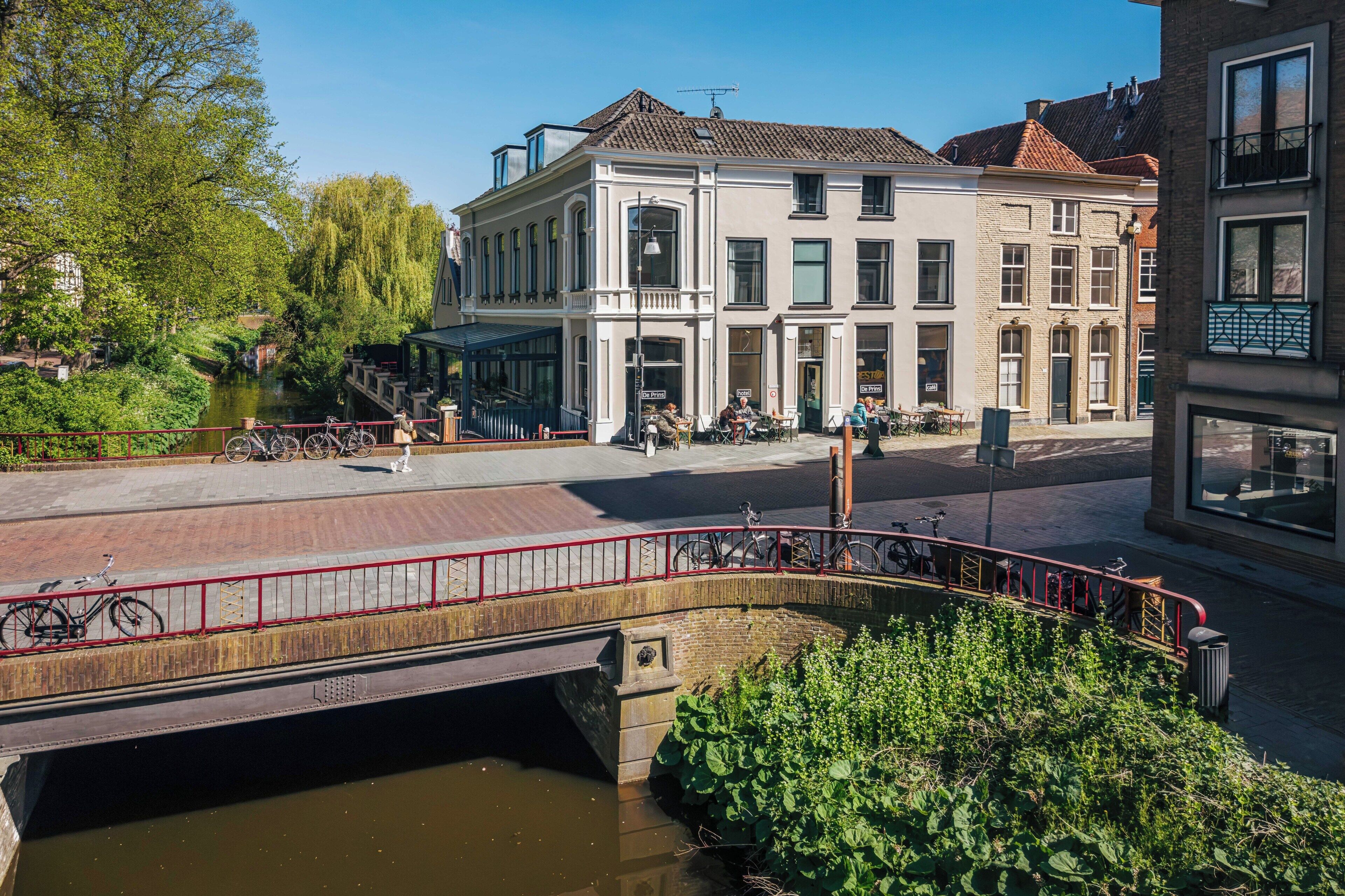 A riverside walkway with a bridge, a row of buildings with large windows, and a clear sky.