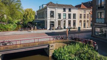 A riverside walkway with a bridge, a row of buildings with large windows, and a clear sky.