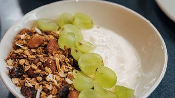 Uma tigela de iogurte com granola e uvas, um croissant e fatias de pão sobre uma mesa.