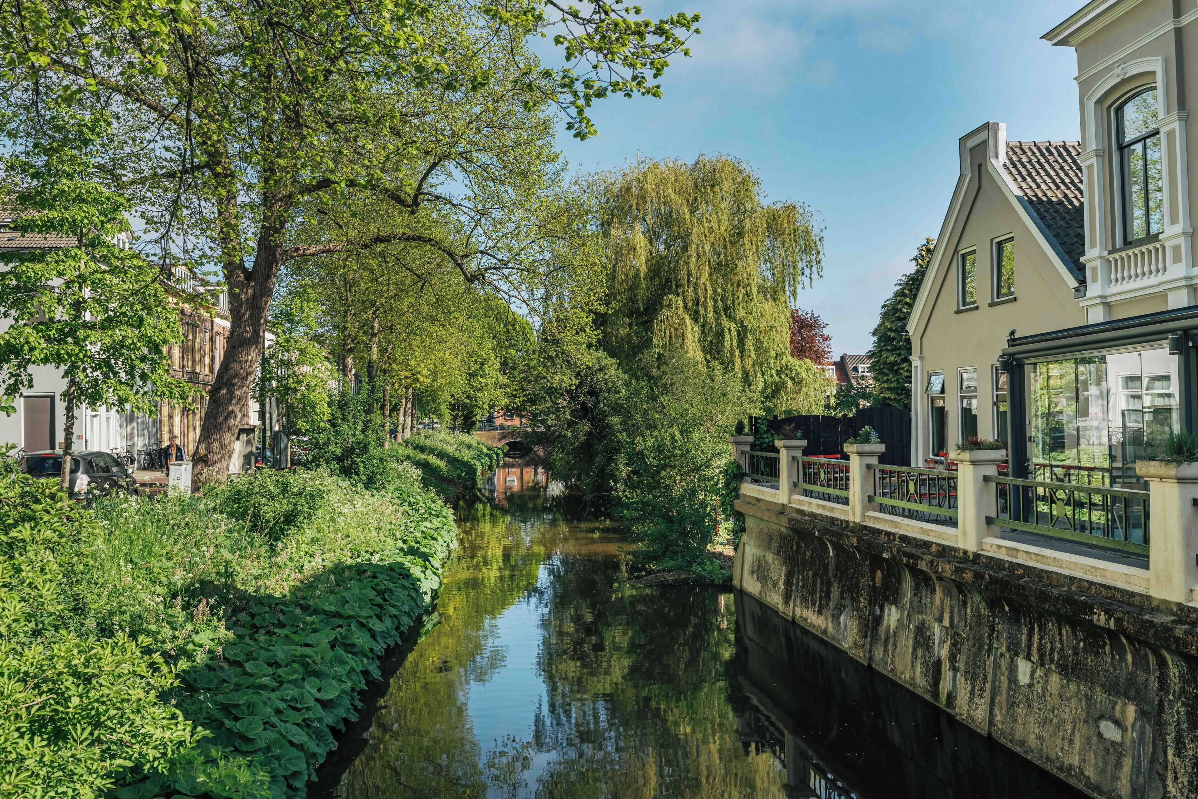 Een gracht met een brug, weelderige begroeiing en een gebouw met een balkon.