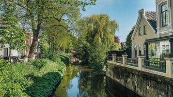 Een gracht met een brug, weelderige begroeiing en een gebouw met een balkon.