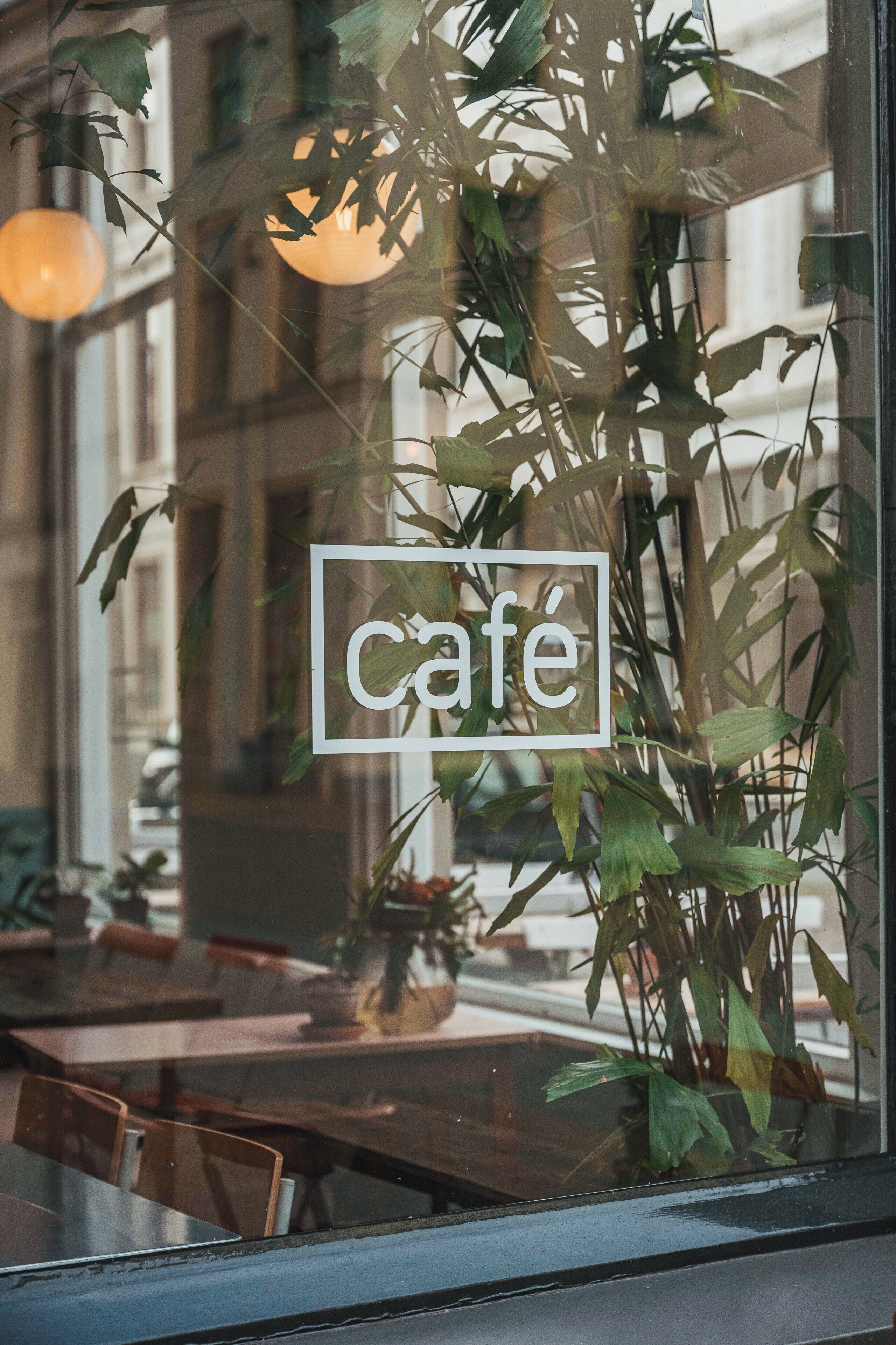 A cafe with a glass window, indoor plants, and a sign with the word 'cafe'.