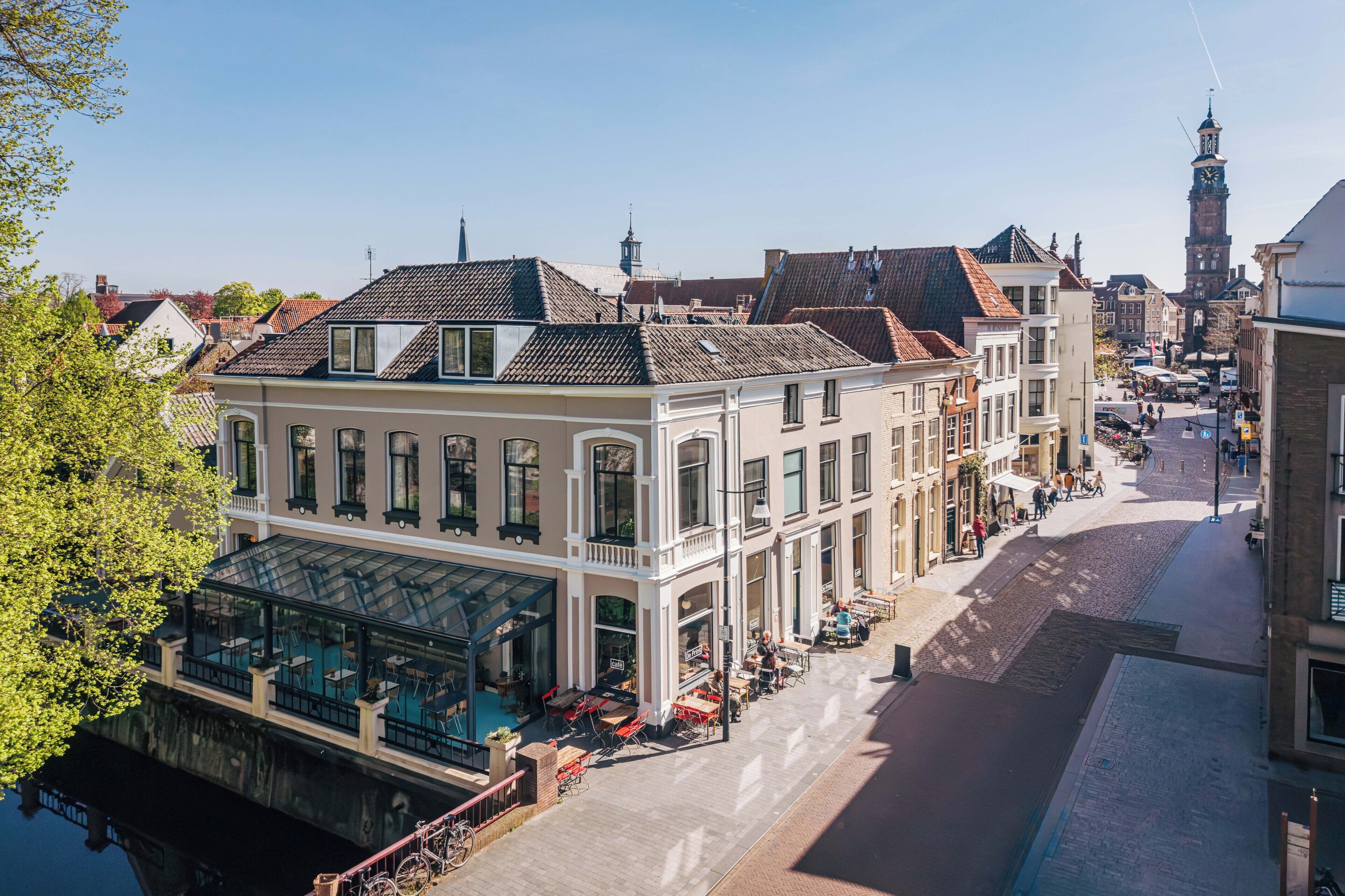 A historic building with a glass conservatory, outdoor seating, and a cobblestone street.