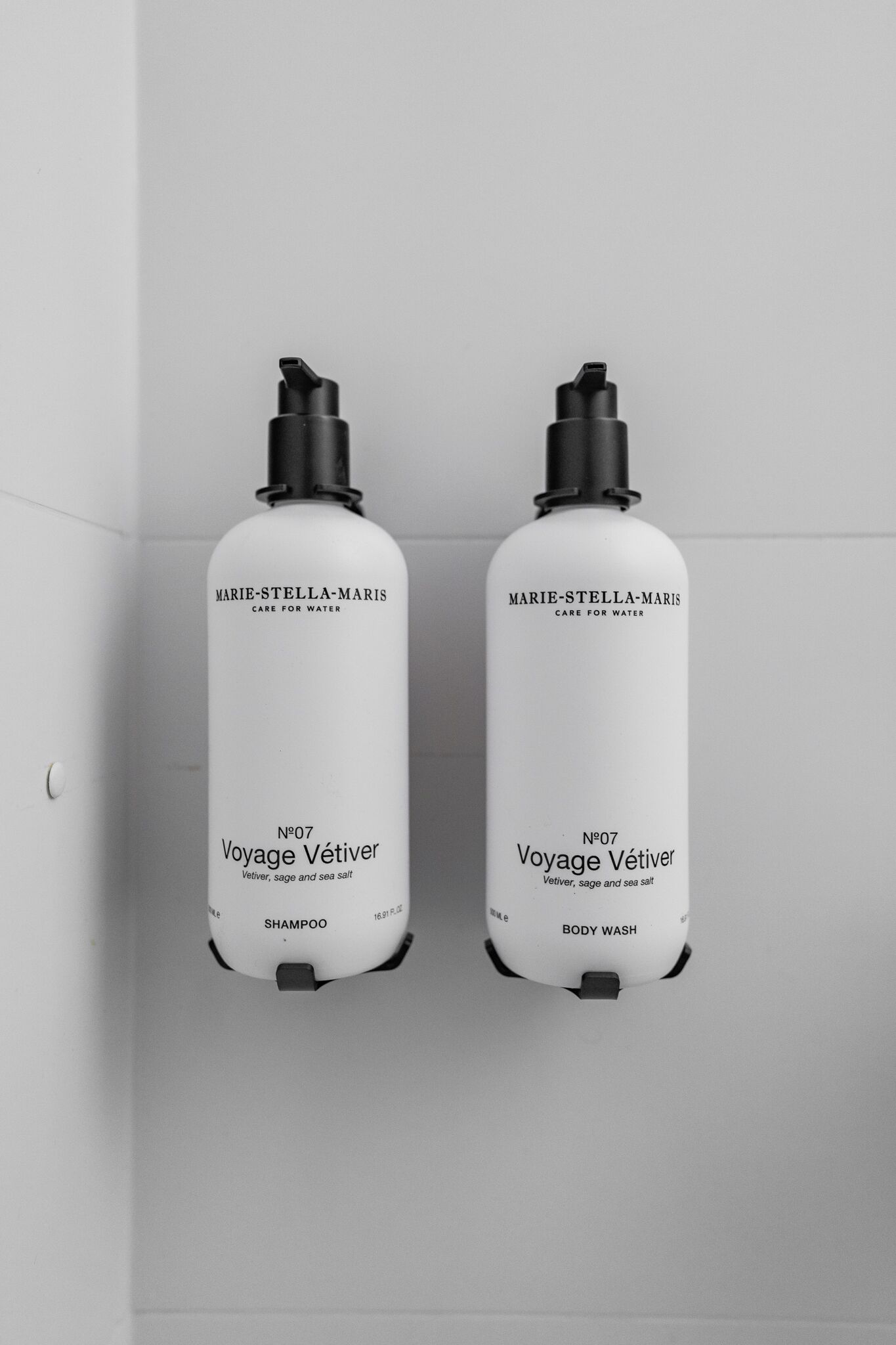 Dos botellas blancas con la etiqueta 'Marie-Stella-Maris' y la inscripción 'Voyage Vétiver' sobre una pared blanca.
