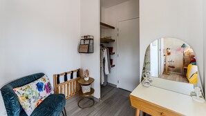Een kamer met een donkergroene stoel, een klein, rond tafeltje met een mand, een spiegel en een houten dressoir.