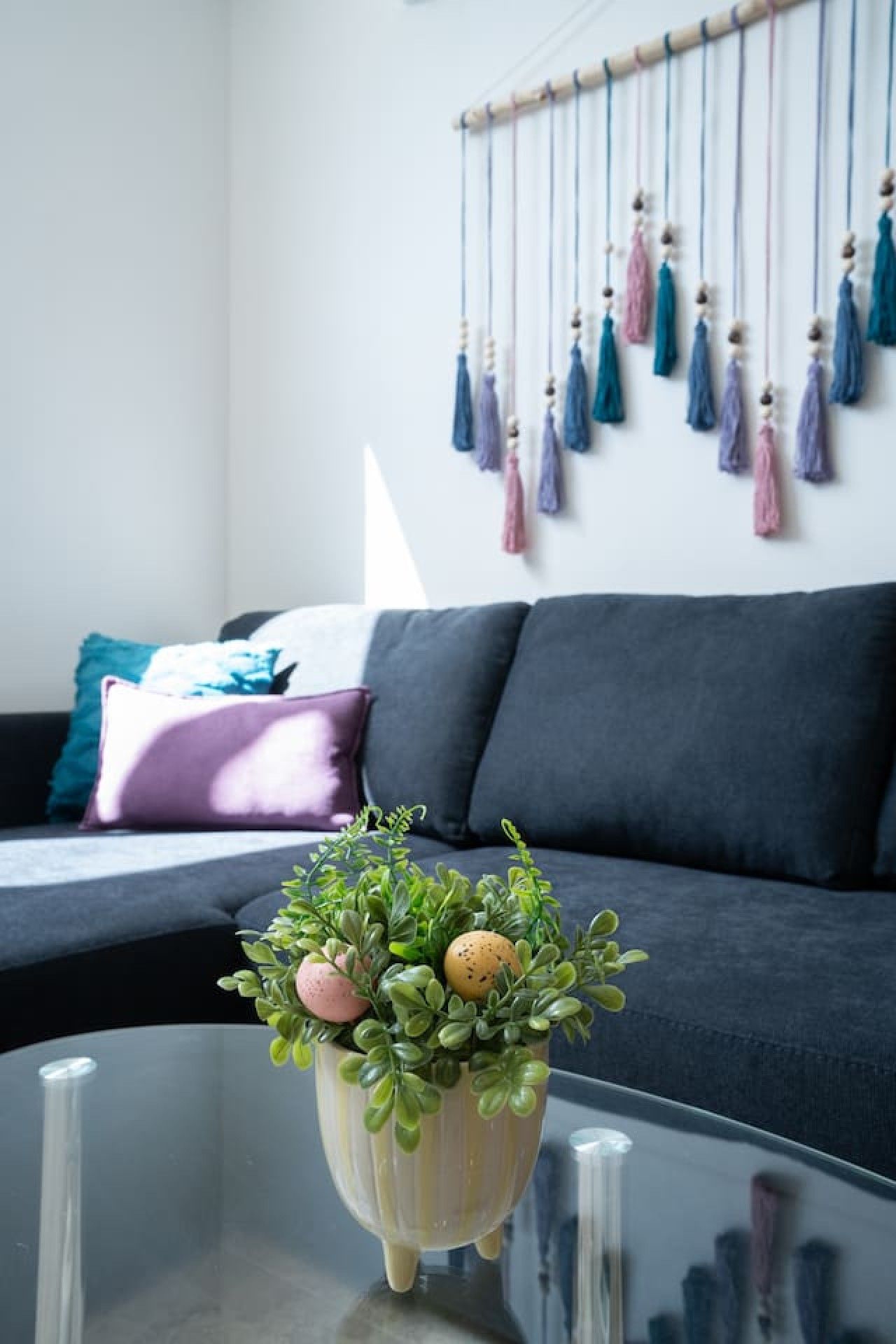 Ein stilvolles Wohnzimmer mit einem dunklen Sofa, einem Glastisch und einer hängenden Quaste.