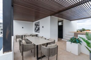 Eine moderne Außenpatio mit einem großen Tisch, Stühlen, einem Metalldach und Topfpflanzen.
