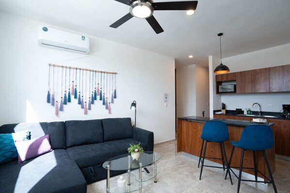 A modern living room with a sofa, a glass coffee table, and a ceiling fan.