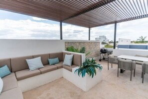 Eine Terrassengruppe mit einem beigefarbenen Ecksofa, einem Esstisch mit Stühlen und einem Grill.