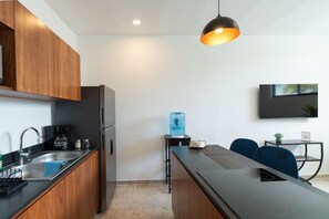 A modern kitchen with wooden cabinets, a stainless steel refrigerator, a water dispenser, and a dining area with a table and chairs. - Secreto de Montebello by Kanaa | 1 bd 1.5 bth condo in Northen Merida (Merida)
