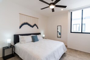 Ein Schlafzimmer mit Bett, Deckenventilator, Wandteppich, Nachttisch mit Lampe und Fenster mit Aussicht.
