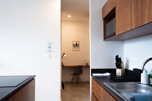 A modern kitchen with a microwave, sink, and knife block. There is a chair and a desk with a lamp in the background.
