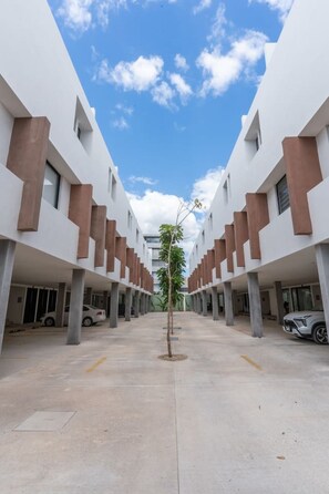 A modern building with a central courtyard, featuring a tree and parked cars. - Atardeceres de Montebello by Kanaa | 1 bd 1.5 bth condo in Northen Merida (Merida)