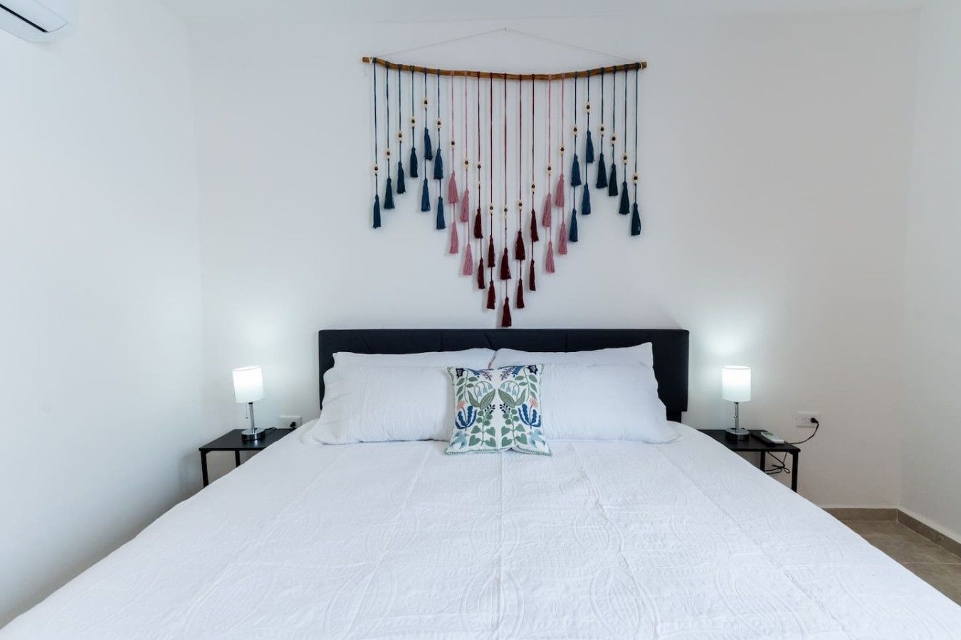 Ein Schlafzimmer mit einem Bett, zwei Nachttischen, einer Wanddekoration und einem Beistelltisch mit Lampe.