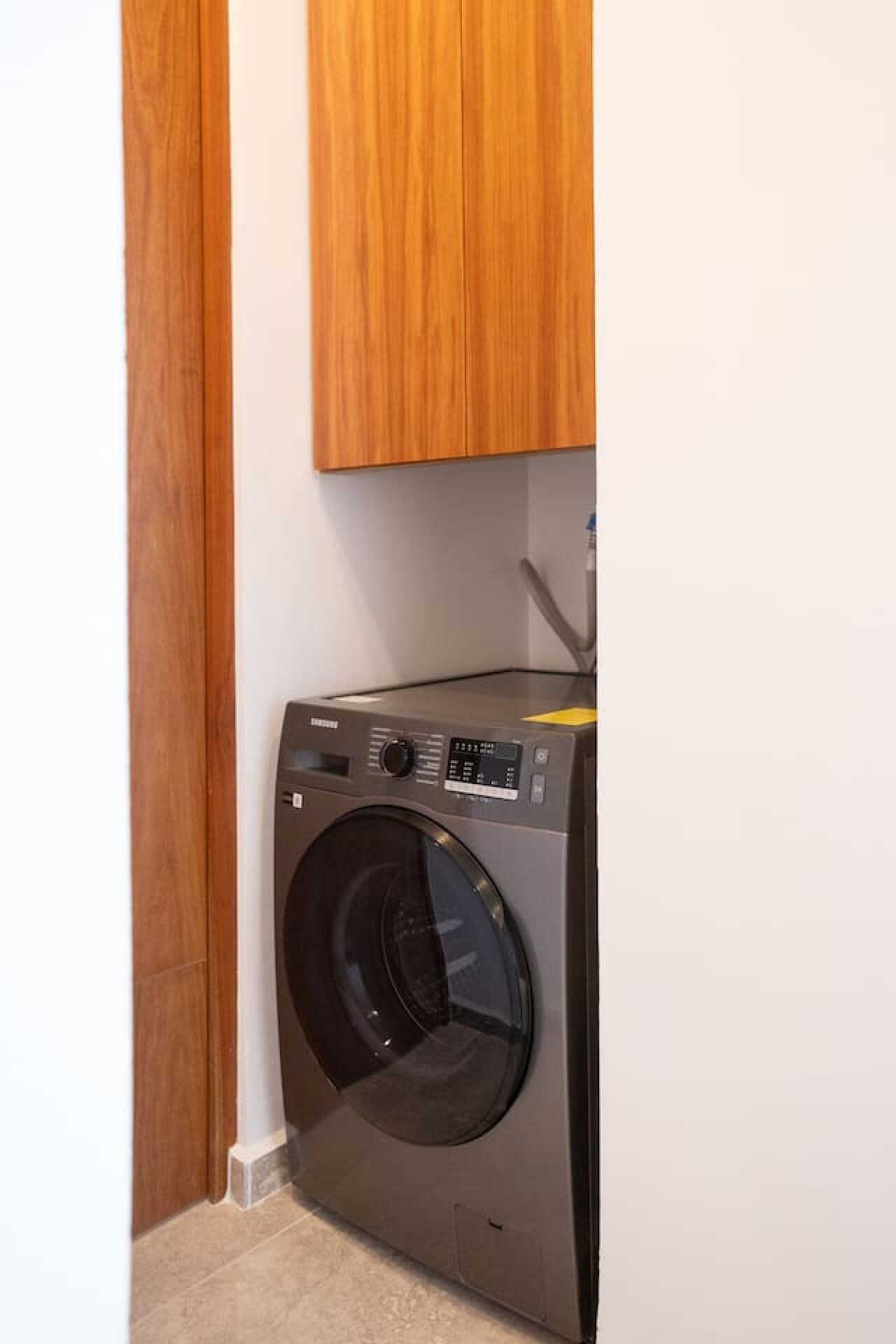 A compact, modern washing machine in a corner of a room with wooden cabinets.