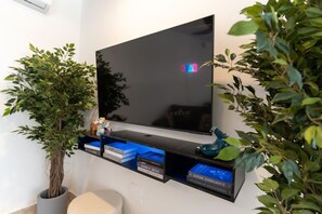 Televisão de tela plana fixada na parede, com uma estante abaixo, contendo livros e objetos decorativos.