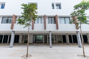A modern building with a flat roof, large windows, and a covered outdoor area with trees. - Atardeceres de Montebello by Kanaa | 1 bd 1.5 bth condo in Northen Merida (Merida)