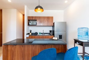 A modern kitchen with wooden cabinets, a black countertop, and a blue water dispenser. - Atardeceres de Montebello by Kanaa | 1 bd 1.5 bth condo in Northen Merida (Merida)