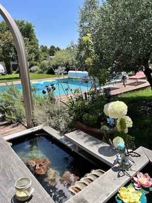 Une piscine avec un jacuzzi, entourée de verdure et dotée d’une terrasse en bois.