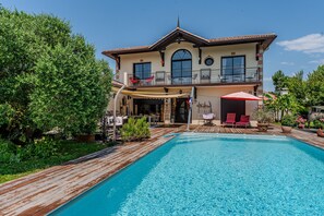 Uma casa de dois andares com piscina, área de estar externa e varanda.