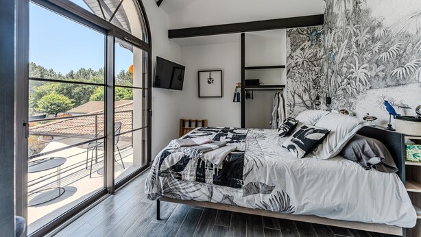 Une chambre avec une grande fenêtre, un lit avec une literie à motifs, un téléviseur à écran plat et une fresque murale.