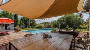 Une terrasse en bois avec une table et des chaises, une piscine et un patio couvert.