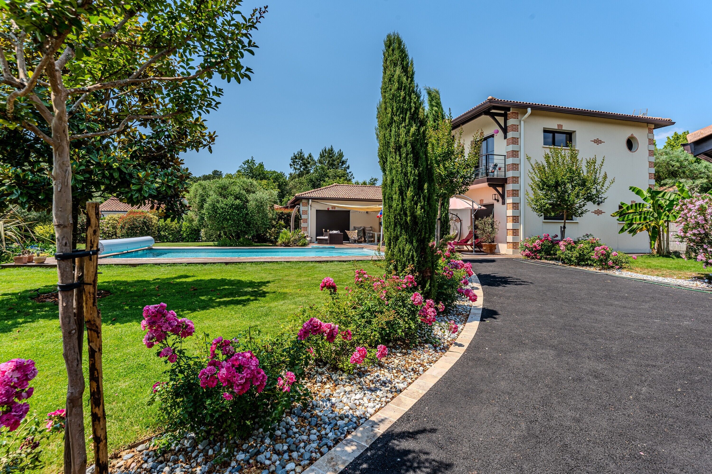 A residential property with a swimming pool, a driveway, and a well-maintained garden with pink flowers.