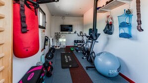 Een fitnessruimte met trainingsapparatuur, een rode bokszak, een blauwe fitnessbal en een loopband.