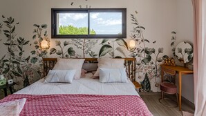 Een slaapkamer met een bed, een raam, een nachtkastje en een bloemen behang wand.