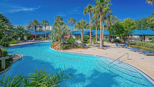 A swimming pool with lounge chairs and palm trees. - Cozy Retreat in the Sky (Destin)