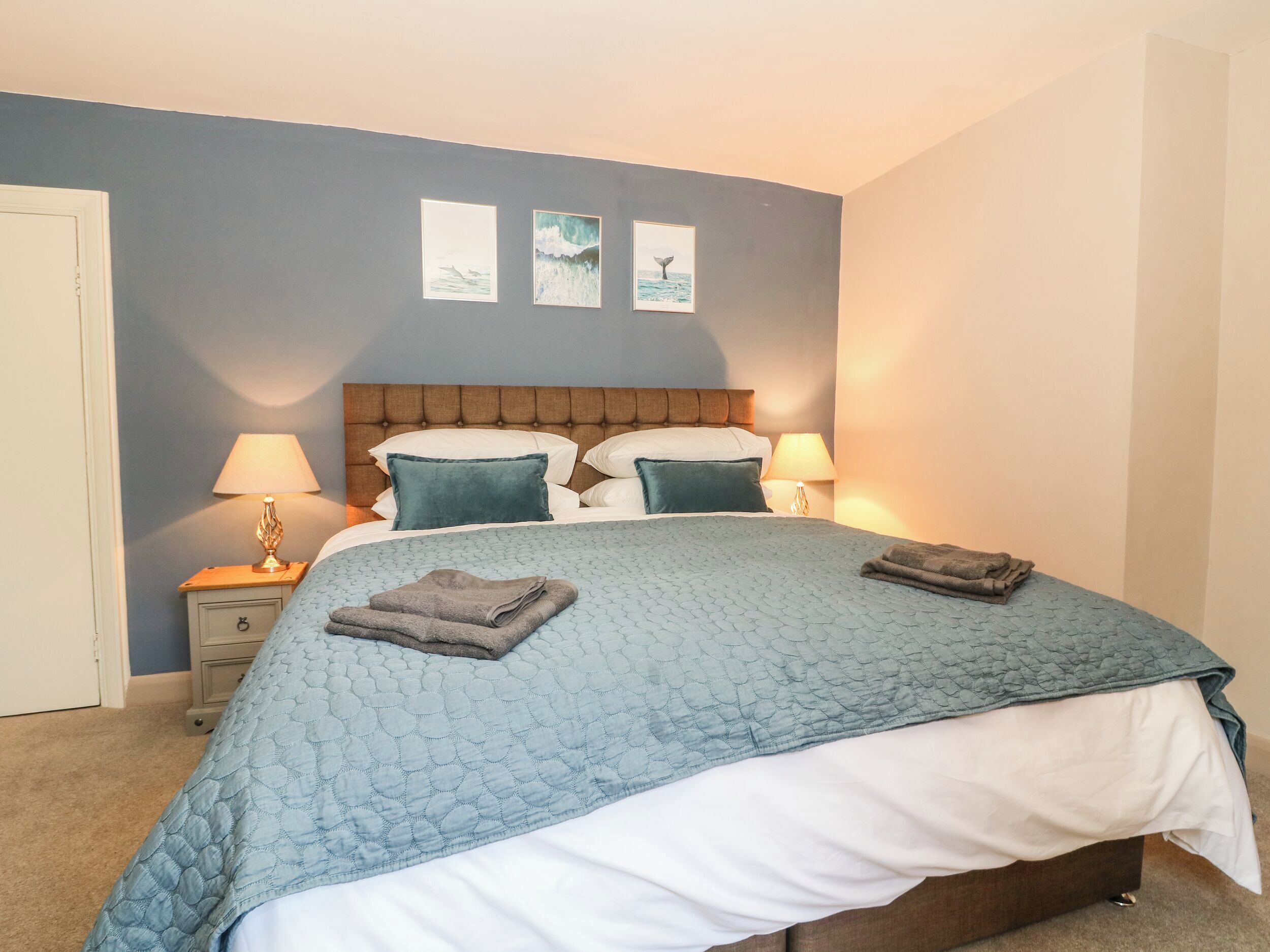 A bedroom with a bed, two bedside tables, a headboard, and three framed pictures on the wall.
