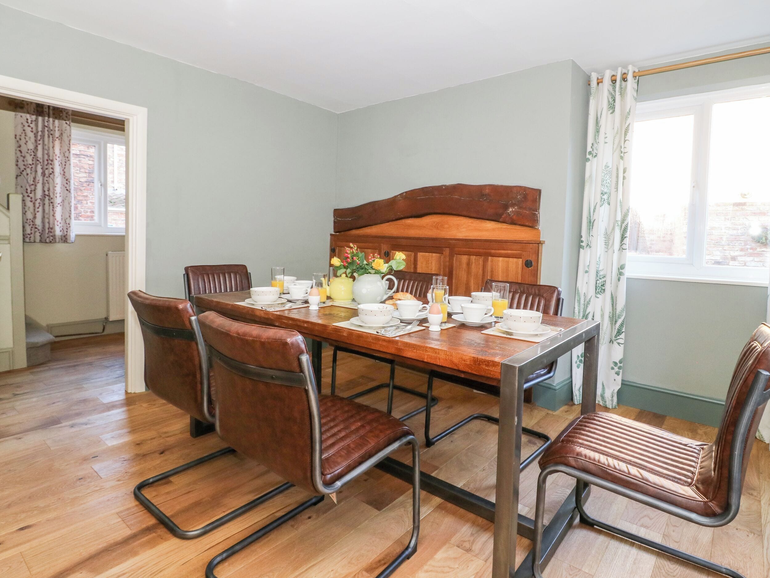 Un comedor con una mesa de madera preparada para el desayuno, rodeado de sillas de cuero y un banco de madera.