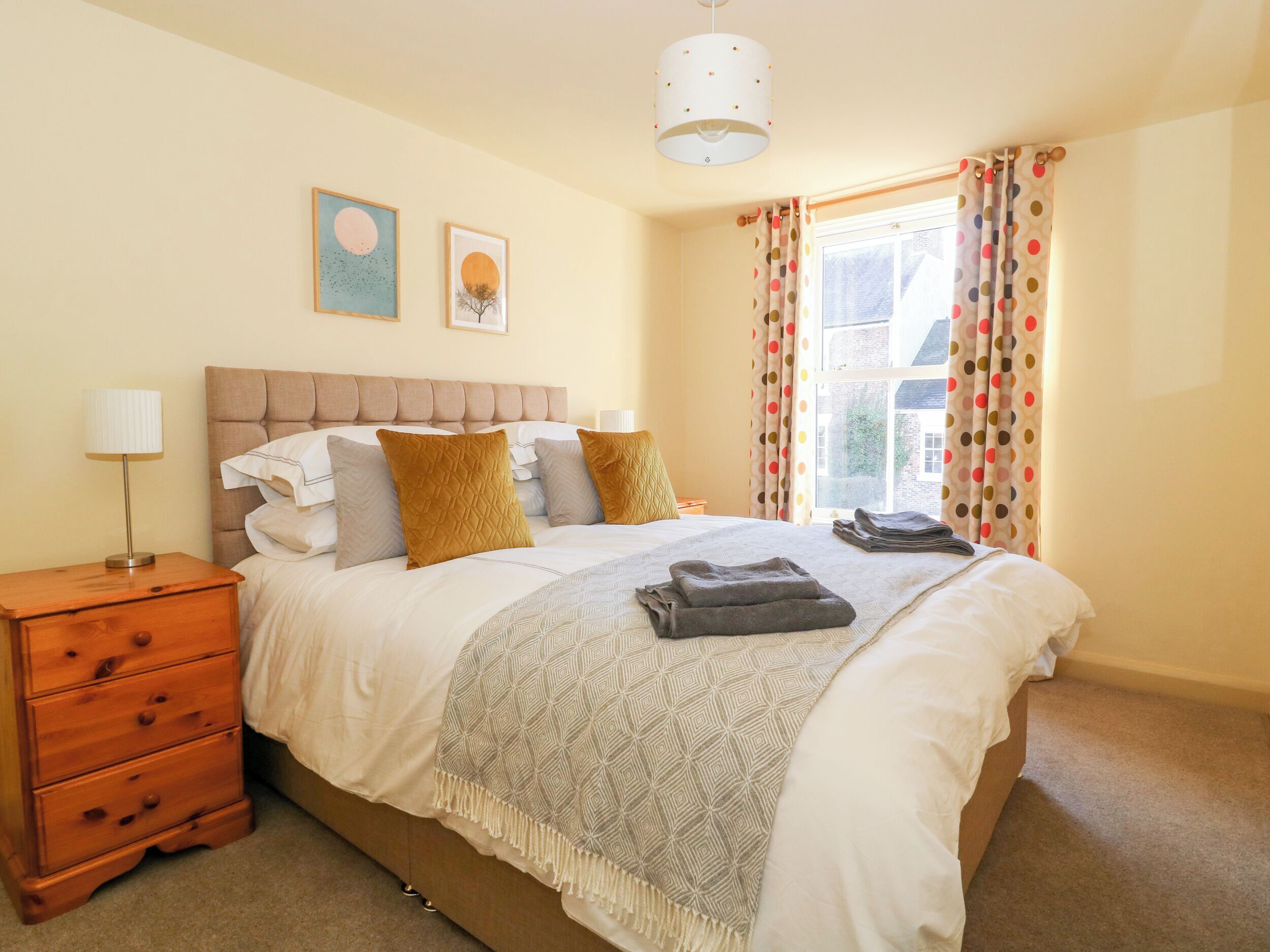 A neatly made bed with a patterned throw, a bedside lamp, and a wooden nightstand with drawers.