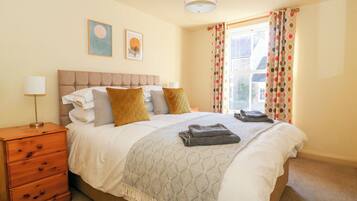 A neatly made bed with a patterned throw, a bedside lamp, and a wooden nightstand with drawers.